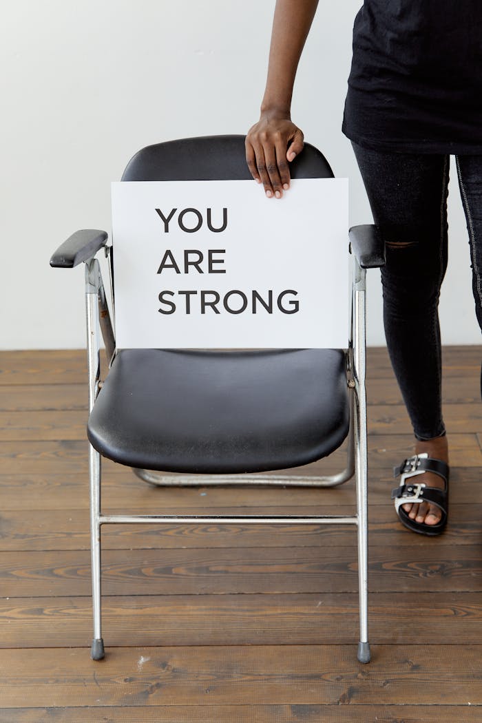 A person holds a card with You Are Strong on a chair, symbolizing support and empowerment.